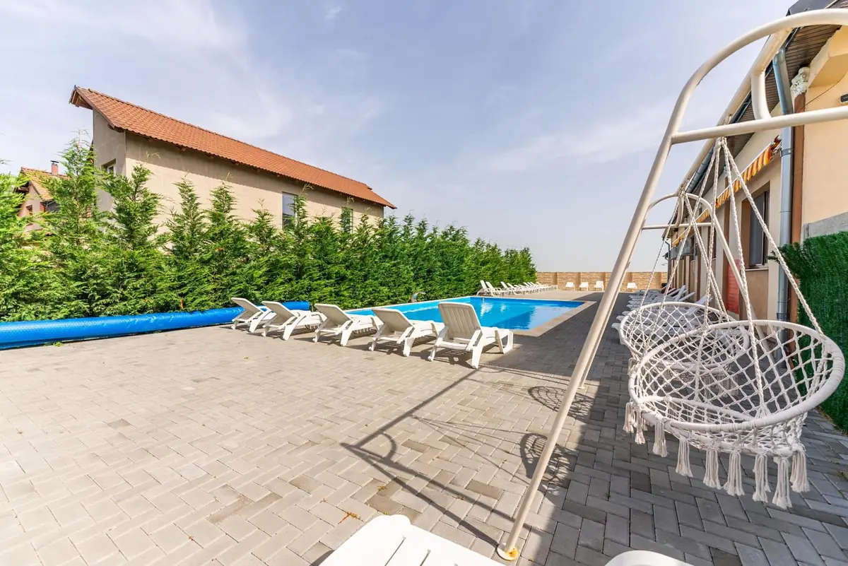 Șezlonguri albe aliniate lângă piscină, cu scaun suspendat tip macramé